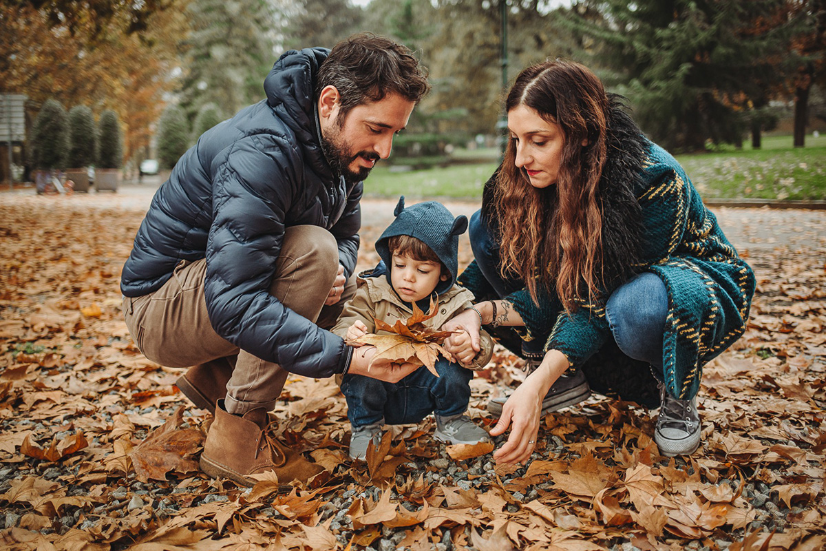 Parco del Valentino, fotografia di famiglia. Sessione fotografica autunnale. Papà mamma e bambino giocano con le foglie autunnali.