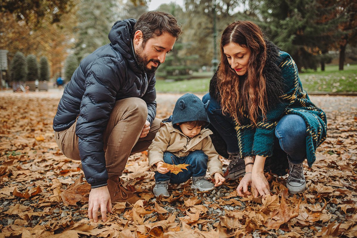 Parco del Valentino, fotografia di famiglia. Sessione fotografica autunnale. Papà mamma e bambino giocano con le foglie autunnali.