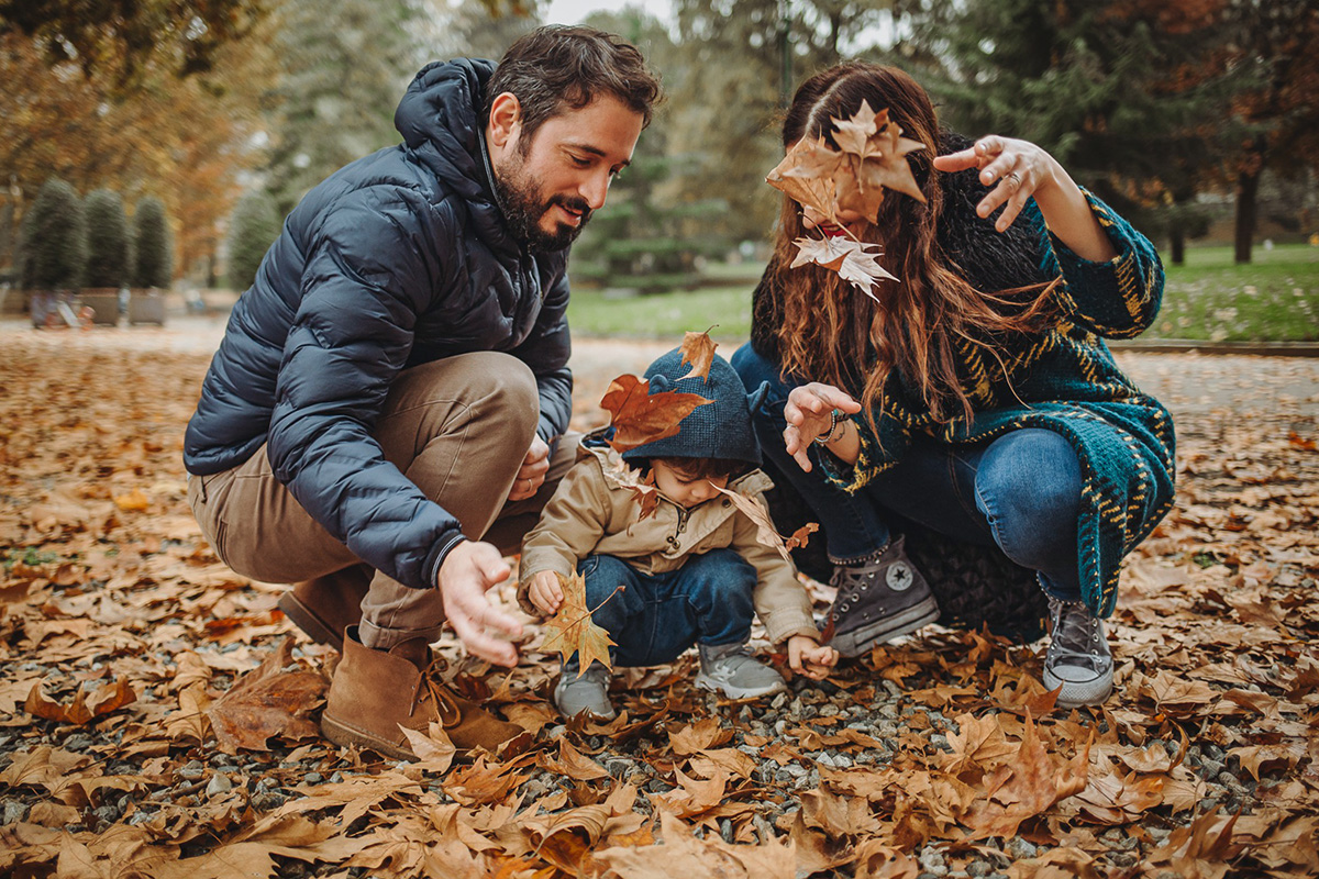 Parco del Valentino, fotografia di famiglia. Sessione fotografica autunnale. Papà mamma e bambino giocano con le foglie autunnali.