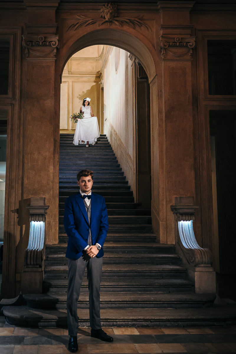 The number 6, Torino, editorial wedding. First look. Sposa che scende lo scalone alle spalle dello sposo.