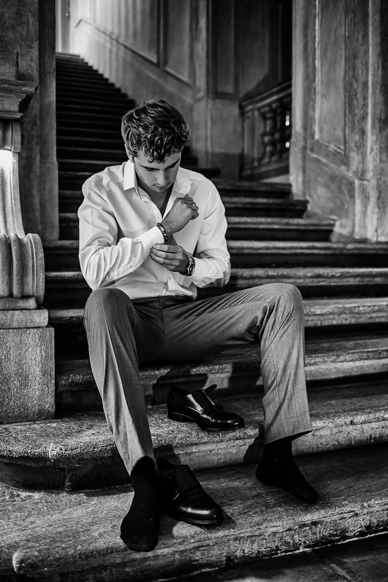 The number 6, Torino, editorial wedding. Preparazione dello sposo.Sposo che si abbottona la camicia seduto sulle scale. Bianco e nero.