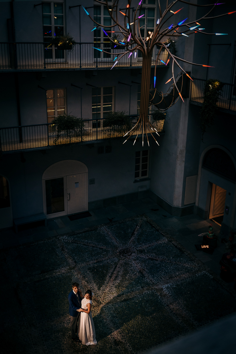 The number 6, Torino, editorial wedding. Ritratto degli sposi dall'alto che si dirigono verso il cortile con il segnapassi illuminato.