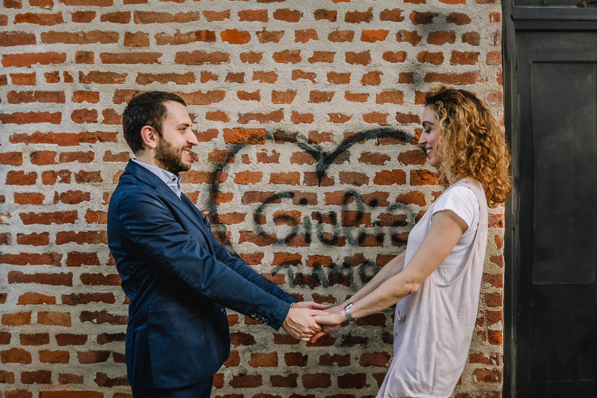 Prematrimoniale nel centro medievale di Chieri. Giulia e Domenico si danno la mano davanti ad una parete di mattoni con un cuore con la scritta Giulia ti amo.