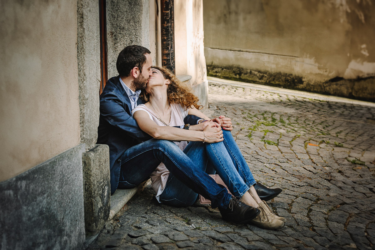 Prematrimoniale nel centro medievale di Chieri. Giulia e Domenico seduti davanti ad un bel portoncino. si baciano.