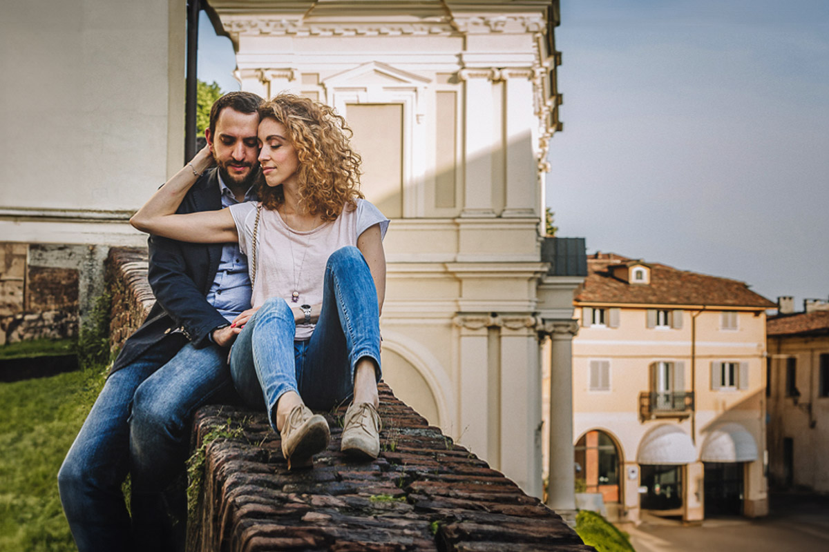 Prematrimoniale nel centro medievale di Chieri. Giulia e Domenico seduti sul muretto con panorama di una bella piazza alle spalle.