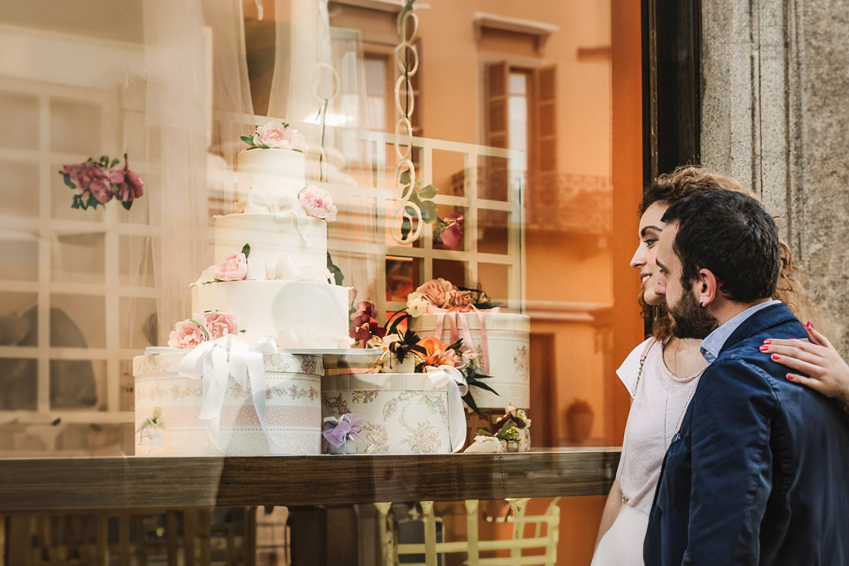 Prematrimoniale nel centro medievale di Chieri. Giulia e Domenico guardano la vetrina di una pasticceria dove è esposta una torta nuziale.