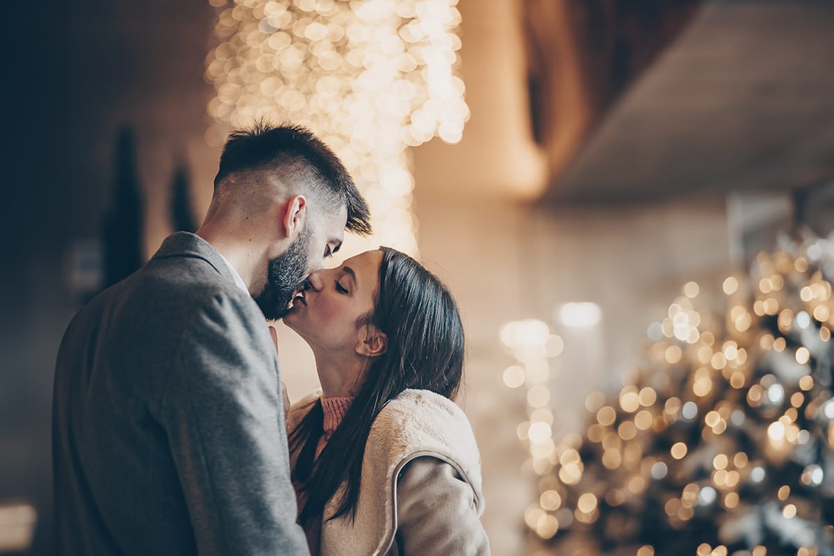 Servizio fotografico di coppia natalizio nel centro di Torino. Coppia davanti alla Rinascente con gli alberi e le luci di Natale. Bacio. Bokeh