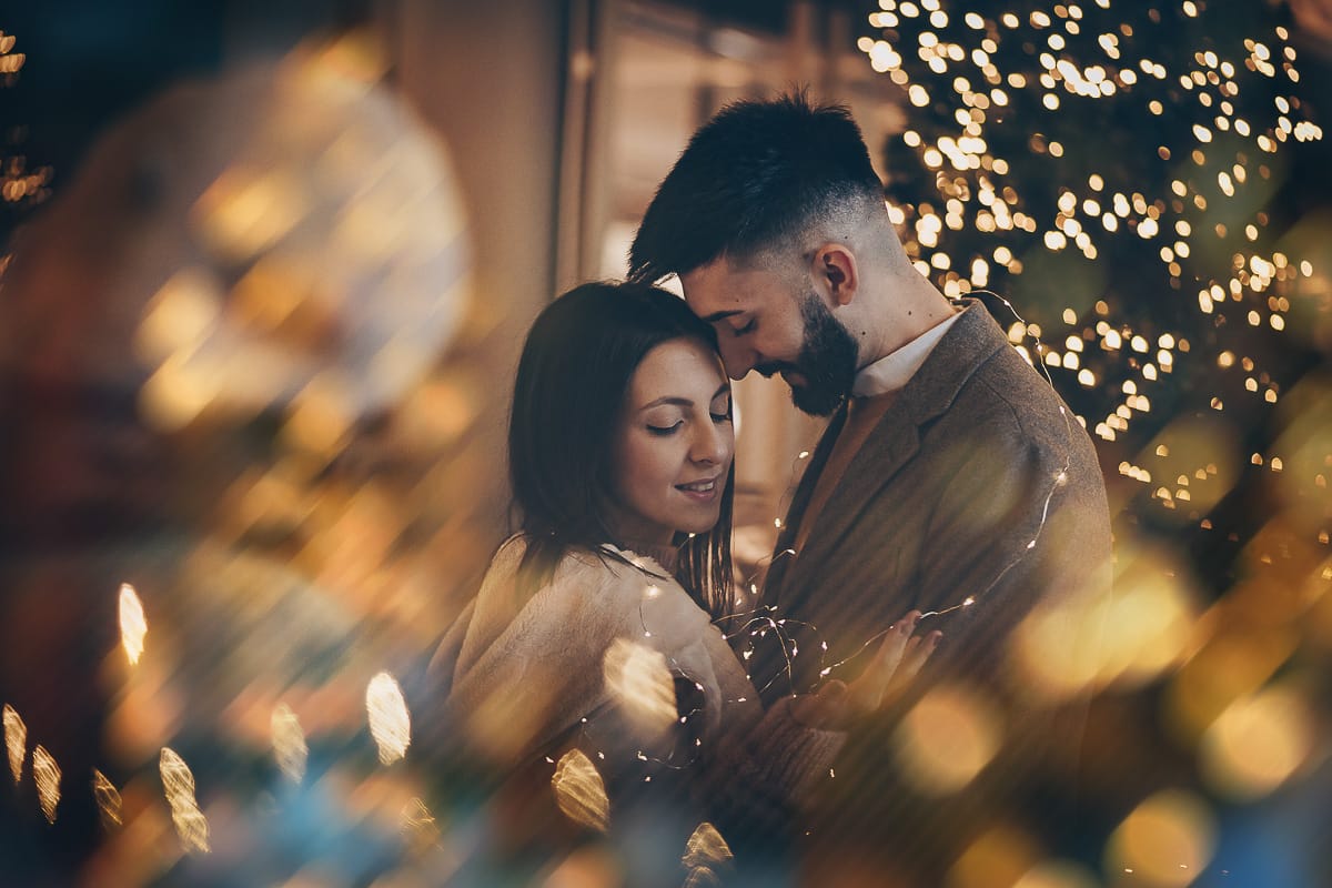 Servizio fotografico di coppia natalizio nel centro di Torino. Coppia davanti alla Rinascente con gli alberi e le luci di Natale.
