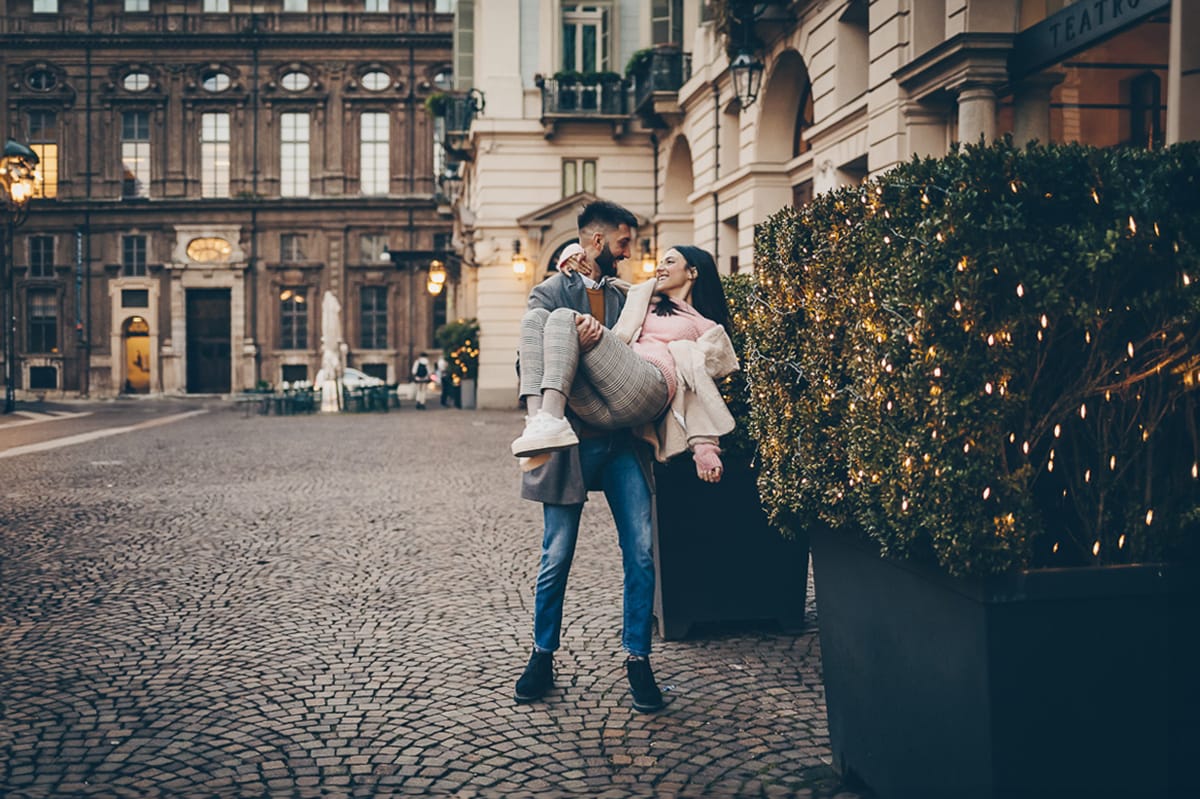 Servizio fotografico di coppia natalizio nel centro di Torino. Coppia in piazza Carignano. Martino prende Paola in braccio.