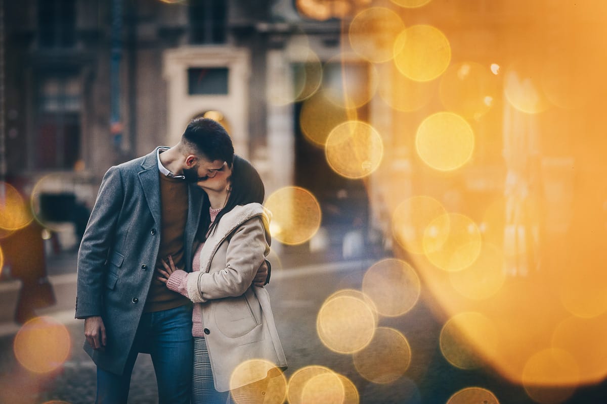 Servizio fotografico di coppia natalizio nel centro di Torino. Coppia in piazza Carignano con le luci natalizie che creano il bokeh. Paola e Martino si baciano.