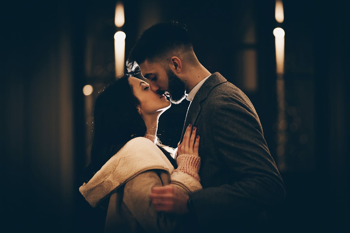 Servizio fotografico di coppia natalizio nel centro di Torino. Coppia in piazza Carignano nell'androne di un palazzo addobbato per Natale. bacio. Flash esterno dietro la coppia.