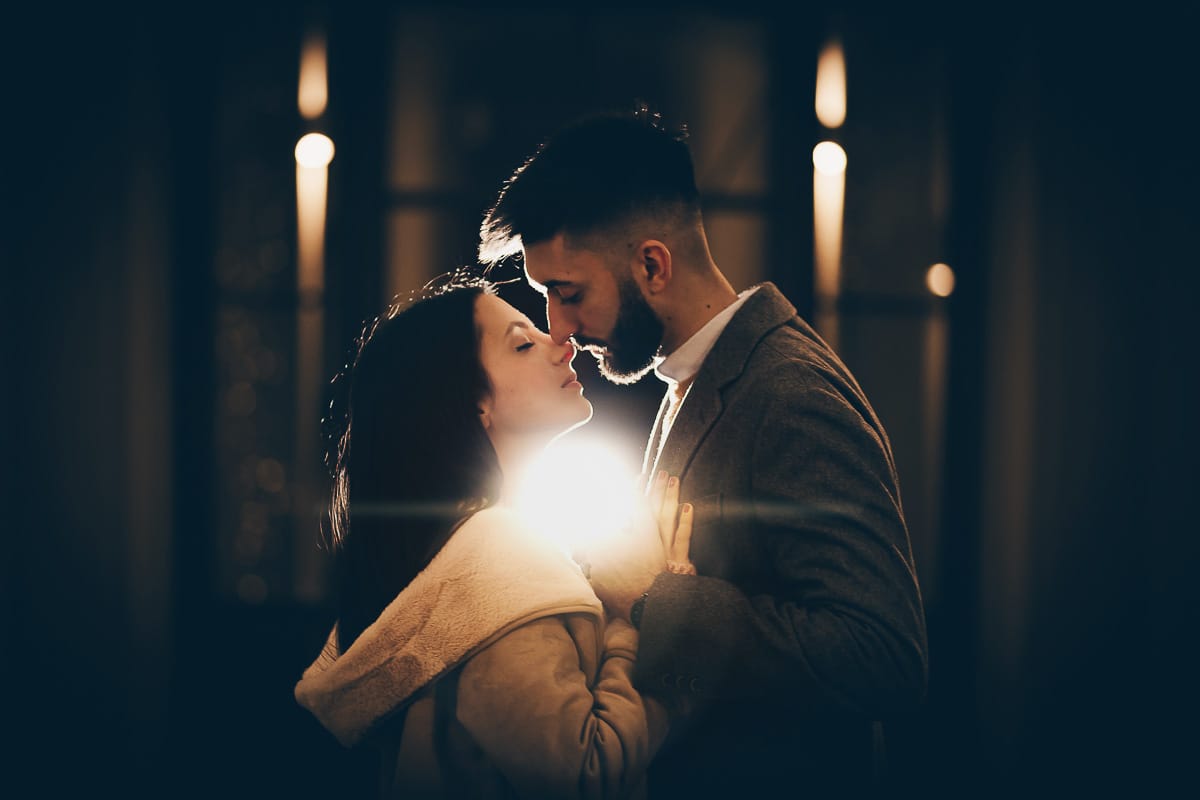 Servizio fotografico di coppia natalizio nel centro di Torino. Coppia in piazza Carignano nell'androne di un palazzo addobbato per Natale. bacio. Flash esterno dietro la coppia.