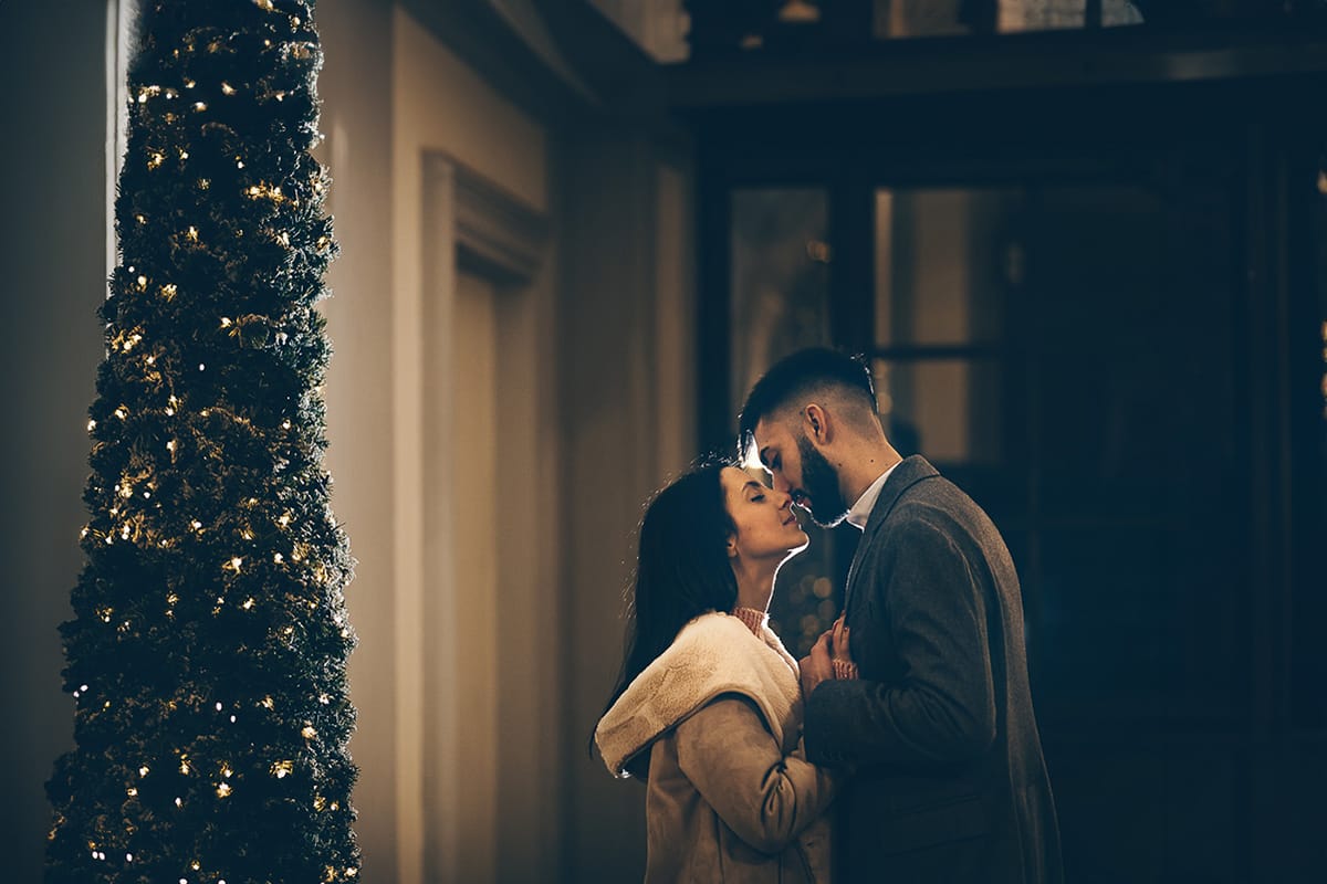 Servizio fotografico di coppia natalizio nel centro di Torino. Coppia in piazza Carignano nell'androne di un palazzo addobbato per Natale. bacio. Flash esterno dietro la coppia.