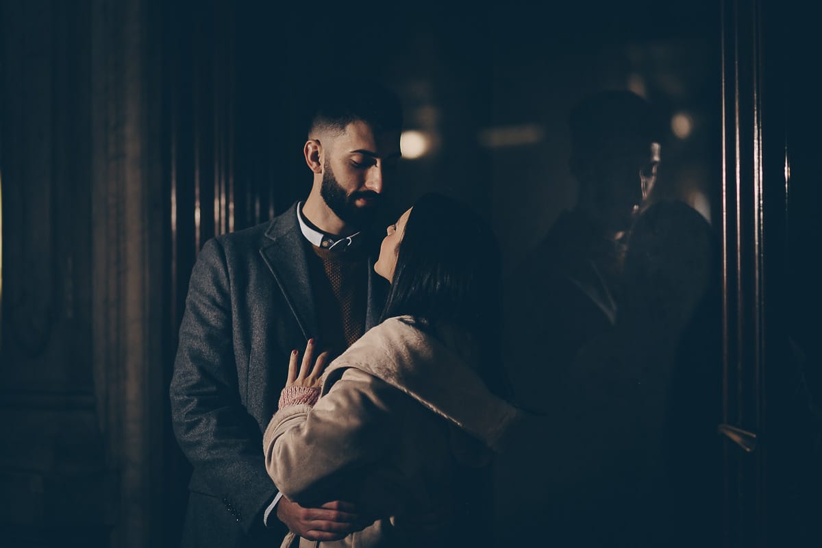 Servizio fotografico di coppia natalizio nel centro di Torino. Coppia in piazza Carignano nell'androne di un palazzo addobbato per Natale. bacio. Flash esterno dietro la coppia.