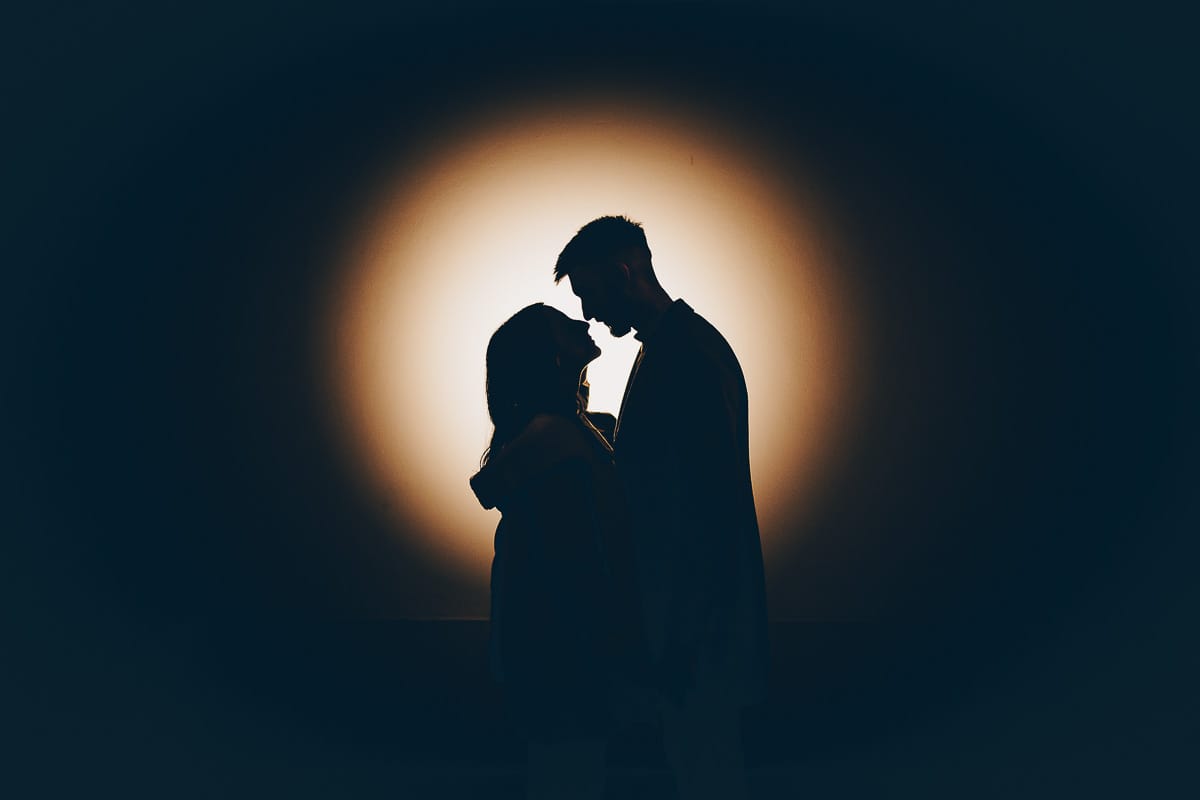 Servizio fotografico di coppia natalizio nel centro di Torino. Coppia in piazza Carignano nell'androne di un palazzo addobbato per Natale. bacio. Flash esterno dietro la coppia puntato sul muro. creazione di una silhouette.