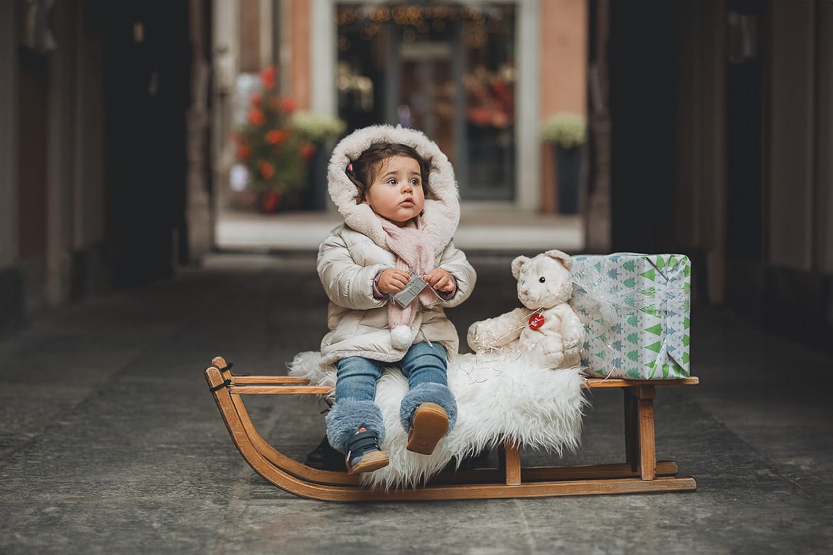 Fotografia di famiglia lifestyle di Natale. La piccola Lavinia seduta su di un vecchio slittino di legno addobbato c