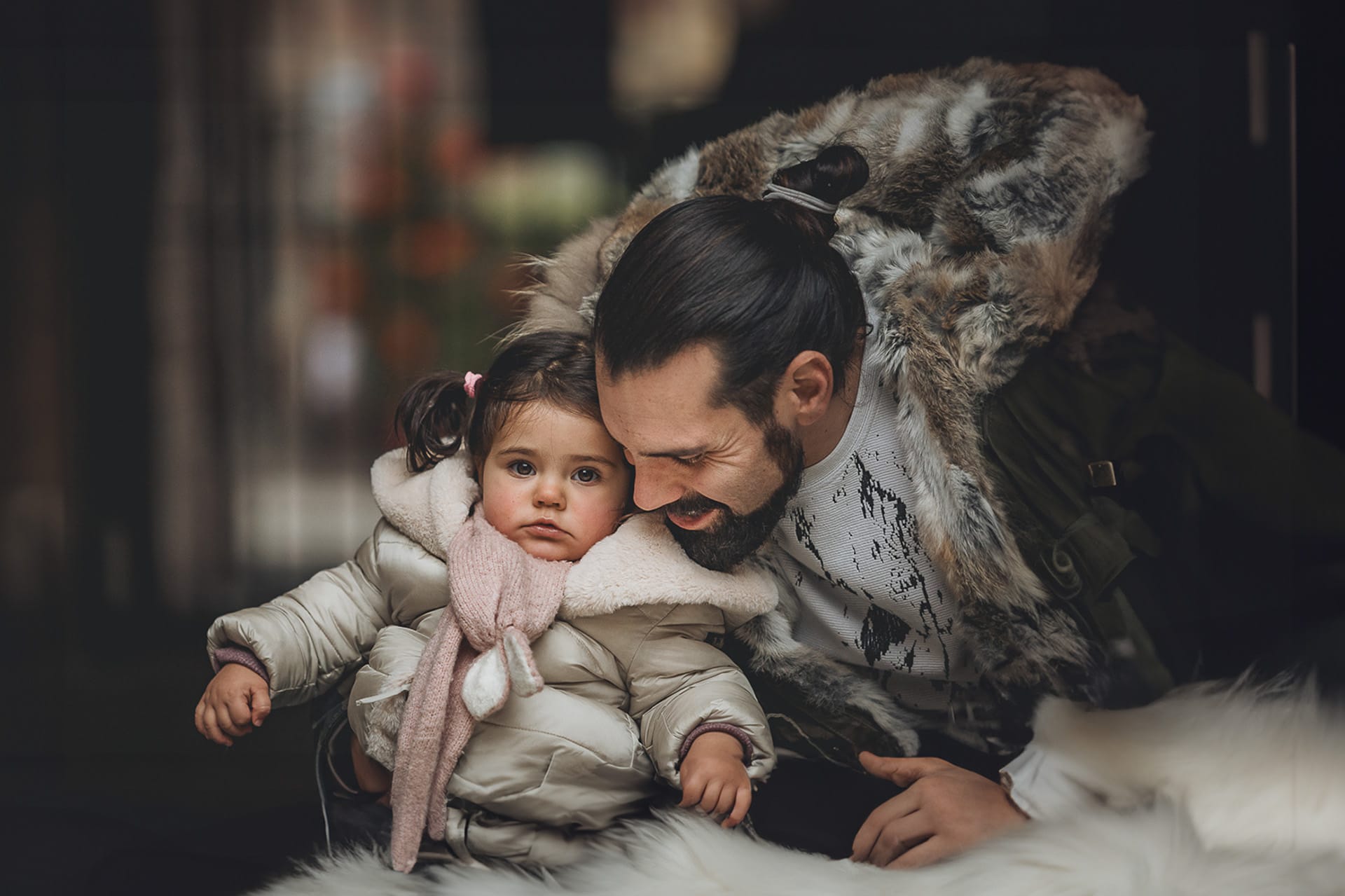 Fotografia di famiglia lifestyle di Natale. La piccola Lavinia con il papà e un vecchio slittino di legno addobbato con un pellicciotto di lana di agnello bianco e pacchi regalo natalizi.