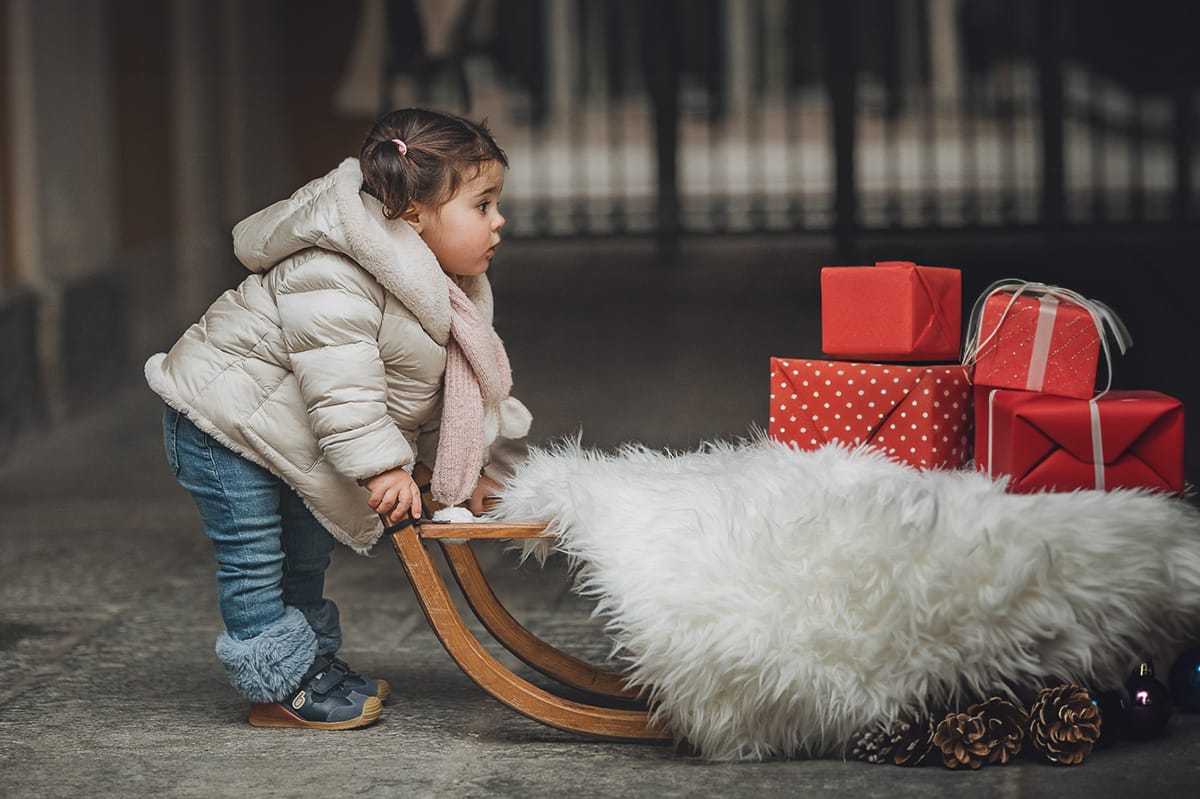 Fotografia di famiglia lifestyle di Natale. La piccola Lavinia spinge il vecchio slittino di legno