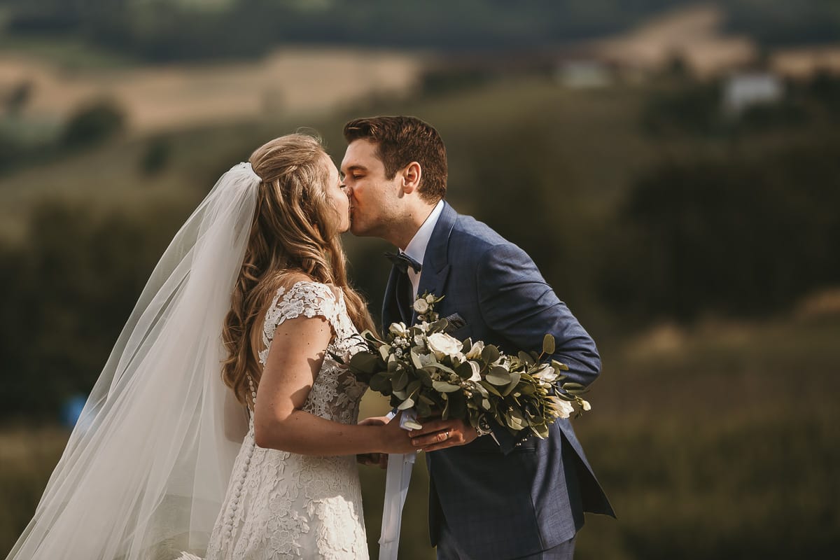 Destination wedding al Relais Sant'Uffizio. Sessione fotografica di coppia. Sposi camminano tra le vigne. Bacio