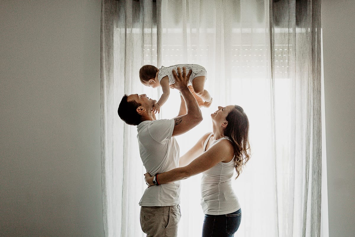 Fotografia di famiglia a Chieri. La piccola Aurora tra le braccia dei genitori davanti ad una finestra