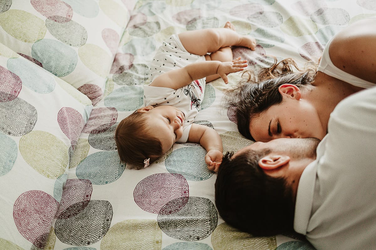 Fotografia di famiglia a Chieri. La piccola Aurora sul lettone con i genitori che si baciano