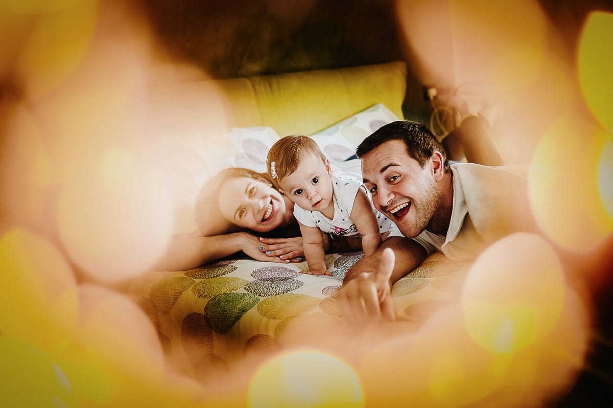 Fotografia di famiglia a Chieri. La piccola Aurora sul lettone con i genitori tra il bokeh delle luci di natale