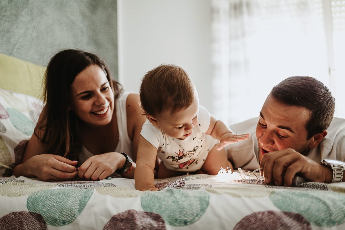 Fotografia di famiglia a Chieri. La piccola Aurora sul lettone con i genitori gioca con le lucine LED