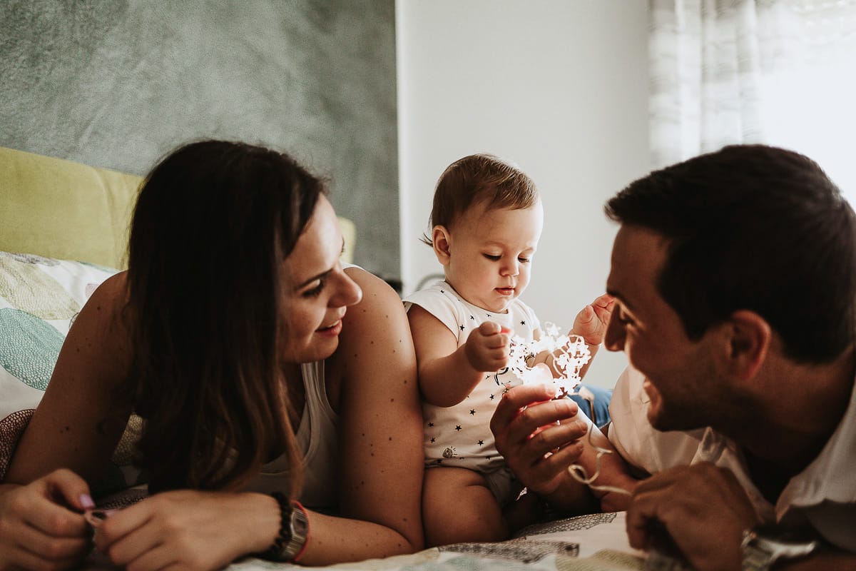 Fotografia di famiglia a Chieri. La piccola Aurora sul lettone con i genitori gioca con le lucine LED