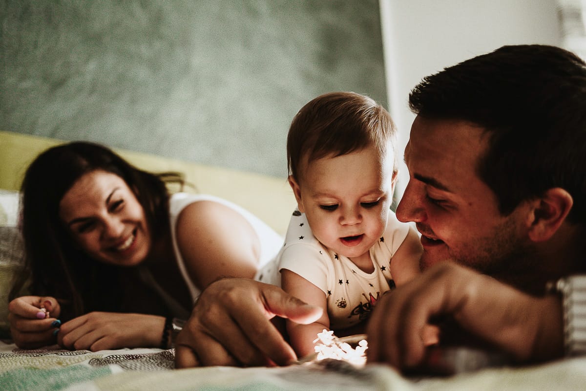 Fotografia di famiglia a Chieri. La piccola Aurora sul lettone con i genitori gioca con le lucine LED