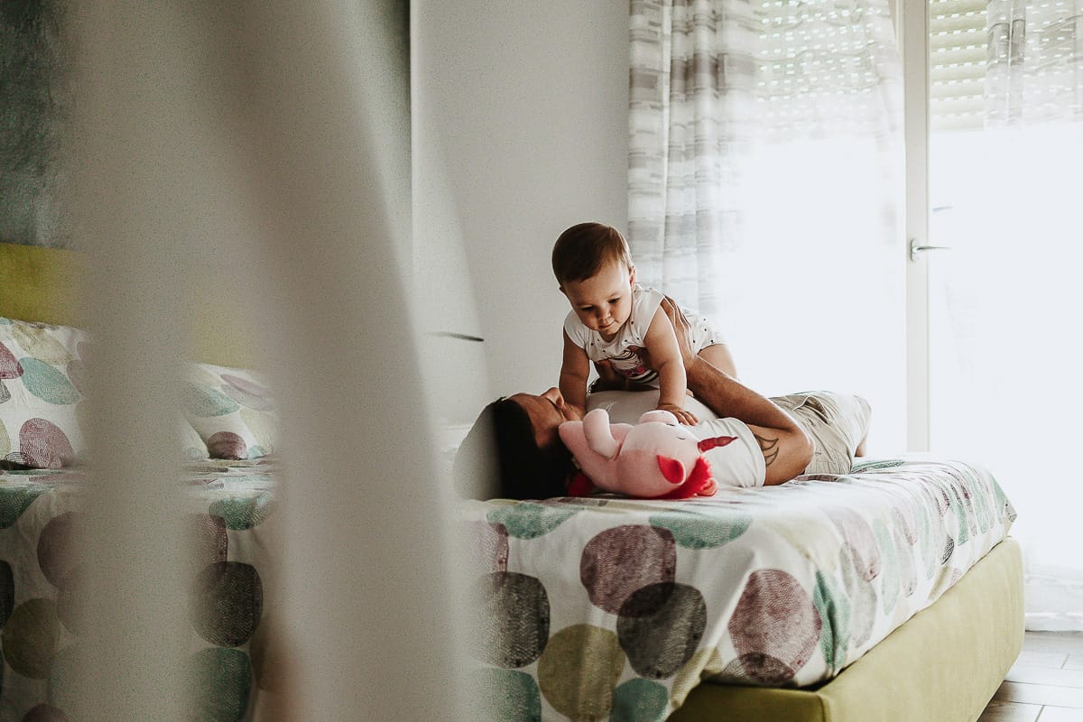 Fotografia di famiglia a Chieri. La piccola Aurora sul lettone sulla pancia del papà