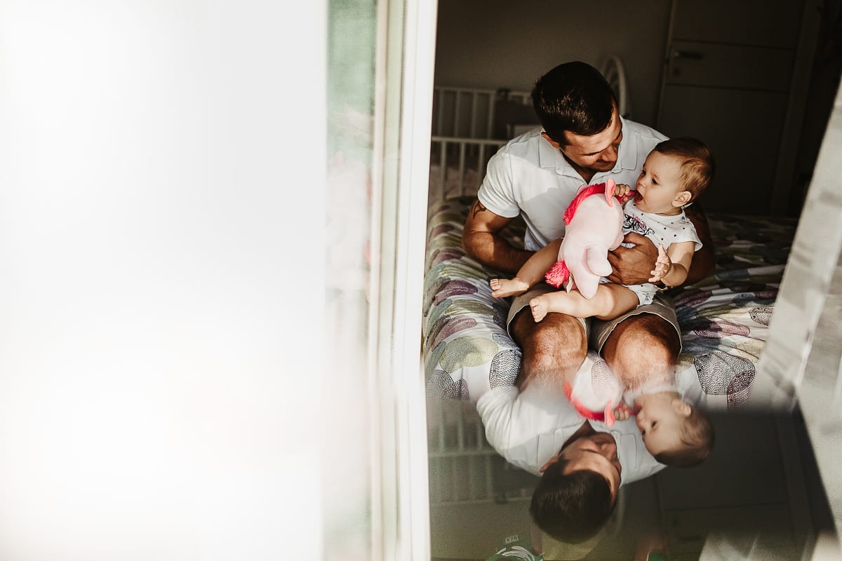 Fotografia di famiglia a Chieri. La piccola Aurora sul lettone in braccio al papà riflessi in uno specchio posto davanti all'obiettivo della fotocamera