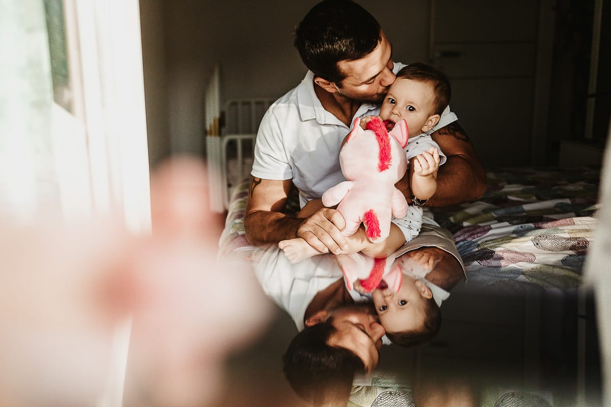 Fotografia di famiglia a Chieri. La piccola Aurora sul lettone in braccio al papà riflessi in uno specchio posto davanti all'obiettivo della fotocamera