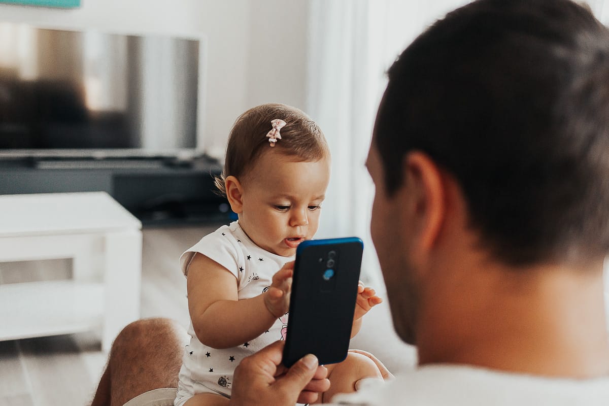 Fotografia di famiglia a Chieri. La piccola Aurora in braccio al papà gioca con il telefono cellulare
