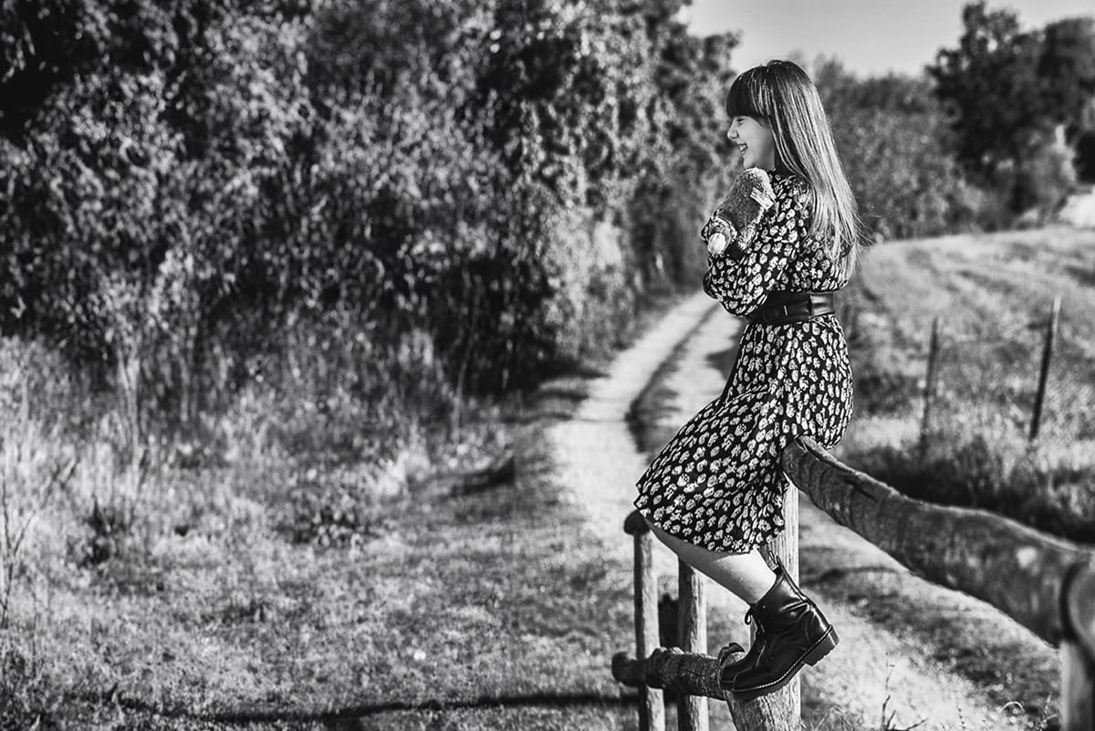 Servizio fotografico di famiglia autunnale in Monferrato. Figlia seduta su di una staccionata di legno