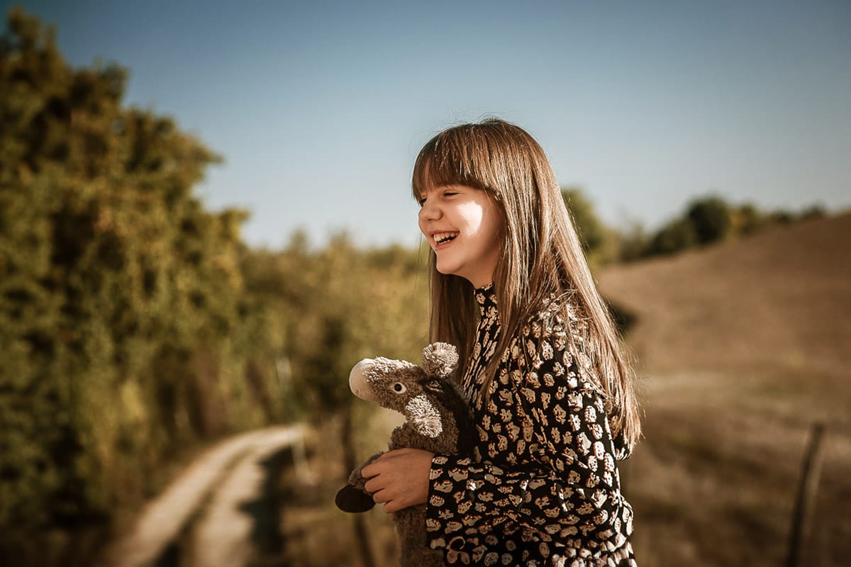 Servizio fotografico di famiglia autunnale in Monferrato. Figlia seduta su di una staccionata di legno con un peluche