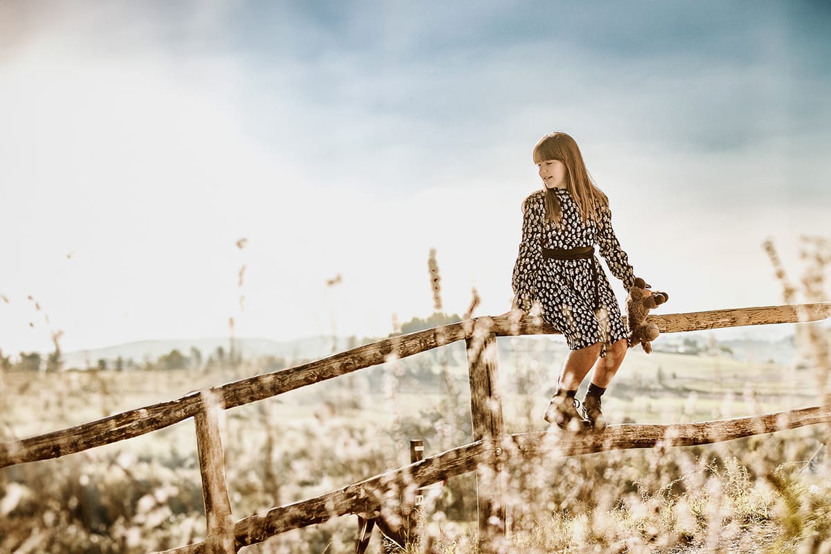 Servizio fotografico di famiglia autunnale in Monferrato. Figlia seduta su di una staccionata di legno