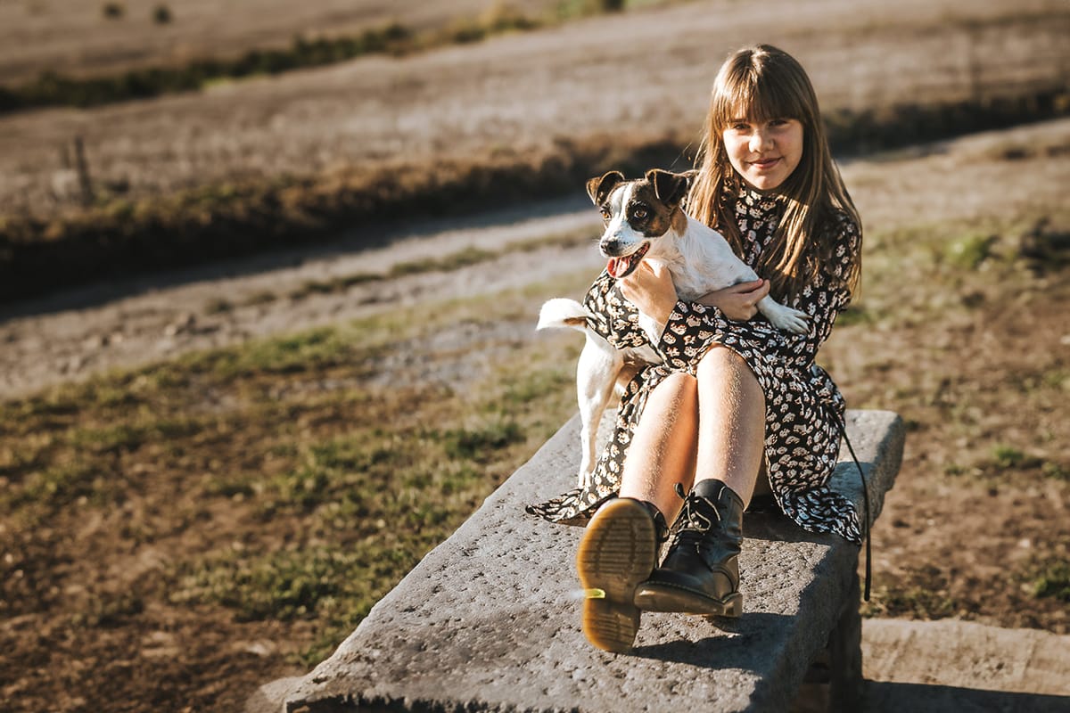 Servizio fotografico di famiglia autunnale in Monferrato. Figlia seduta su di una panchina di pietra ha in braccio la cagnolina jack russell Nina