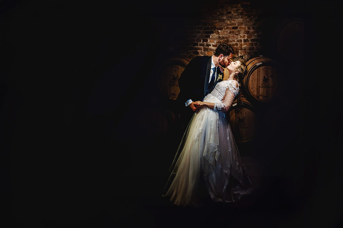 Matrimonio sotto la pioggia a Tenuta Tamburnin di Castelnuovo Don Bosco. Ritratto degli sposi nella cantina dell'azienda vitivinicola con le botti