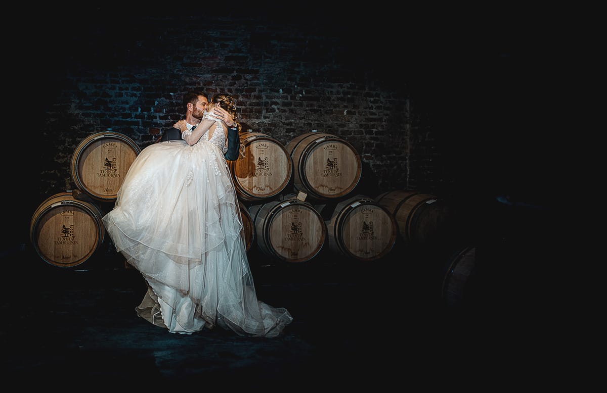 Matrimonio sotto la pioggia a Tenuta Tamburnin di Castelnuovo Don Bosco. Ritratto degli sposi nella cantina dell'azienda vitivinicola con le botti