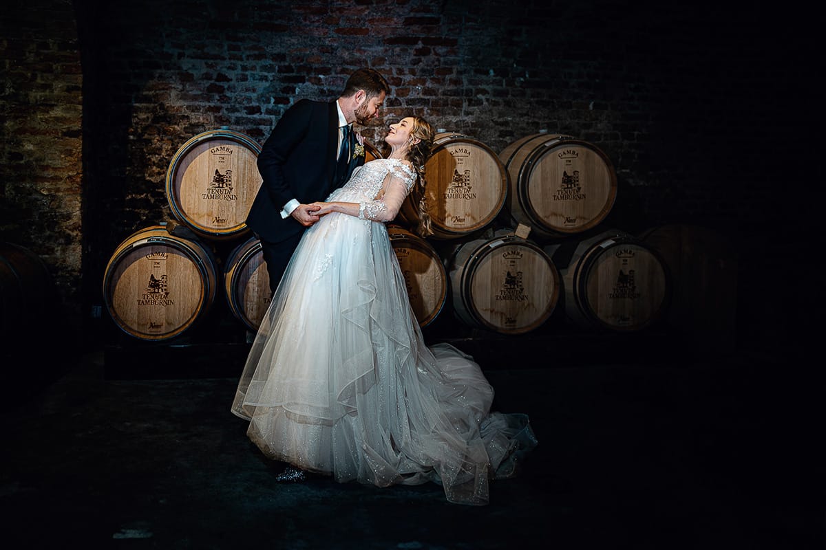 Matrimonio sotto la pioggia a Tenuta Tamburnin di Castelnuovo Don Bosco. Ritratto degli sposi nella cantina dell'azienda vitivinicola con le botti