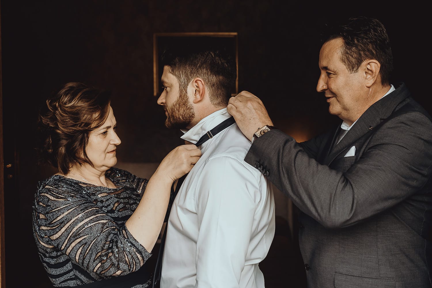 Matrimonio a Cambiano. Preparazione dello sposo. Genitori aiutano lo sposo nella vestizione