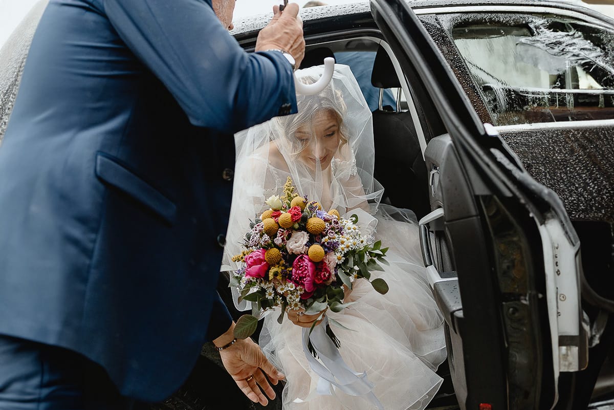 Matrimonio sotto la pioggia a Cambiano. Cerimonia. Sposa esce dall'auto. Padre tiene l'ombrello