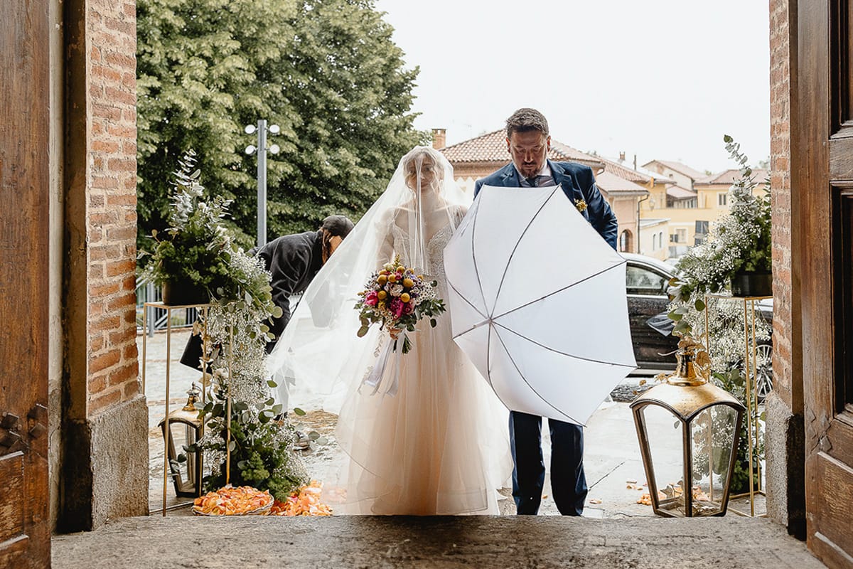 Matrimonio sotto la pioggia a Cambiano. Cerimonia. Sposa davanti all'entrata della chiesa. Padre chiude l'ombrello