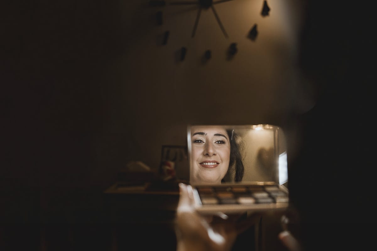 Matrimonio a Riva presso Chieri, preparazione della sposa.Make-up. Sposa riflessa nello specchio della trousse degli ombretti.