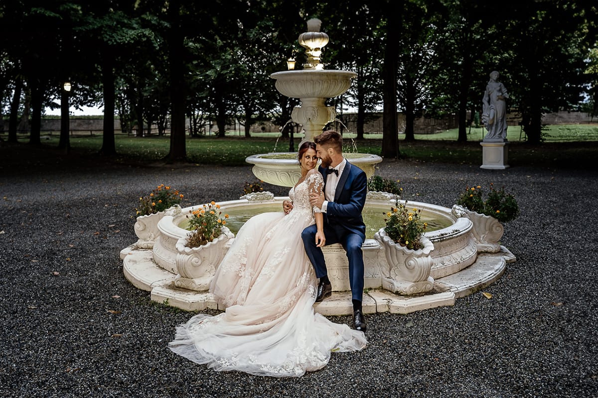 Castello dei Solaro, matrimonio di Noemi e Pietro. Sessione fotografica di coppia. Sposi seduti sulla fontana di pietra bianca. di sera.
