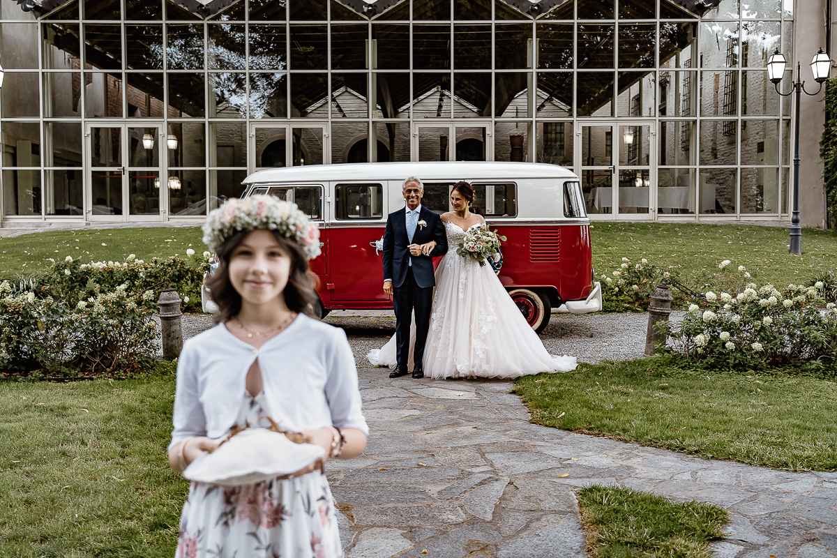 Castello dei Solaro, matrimonio di Noemi e Pietro. Cerimonia. Damigella e dietro sposa con il padre davanti al Van Wolkswagen rosso.