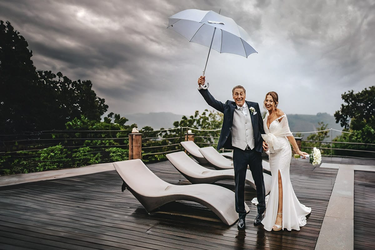 Matrimonio a "La Madernassa" nelle Langhe sotto la pioggia. Ritratti di coppia a bordo piscina sotto un ombrello bianco.