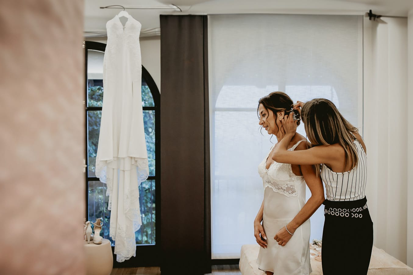 Matrimonio a "La Madernassa" nelle Langhe sotto la pioggia. Preparazione della sposa. Parrucchiera pettina la sposa. Sullo sfondo si vede l'abito da sposa appeso.