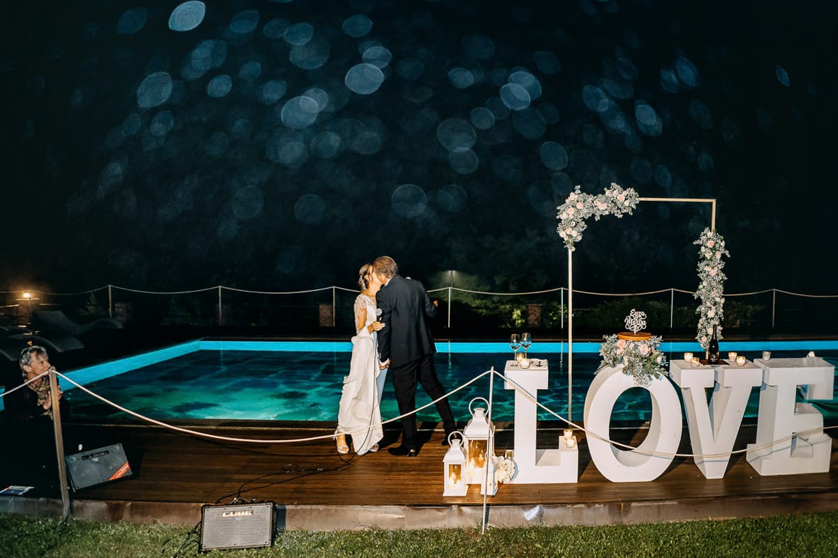 Matrimonio a "La Madernassa" nelle Langhe sotto la pioggia. Taglio torta. Allestimento luminoso, fiori e scritta LOVE. Bacio.