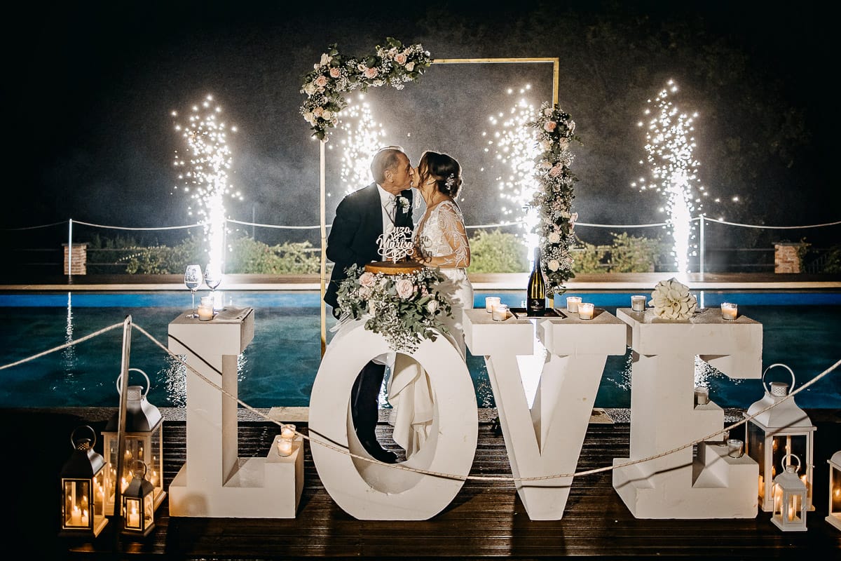 Matrimonio a "La Madernassa" nelle Langhe sotto la pioggia. Taglio torta. Allestimento luminoso, fiori e scritta LOVE. Fontane luminose.
